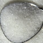 Detailed macro shot of white sugar crystals on a reflective spoon.