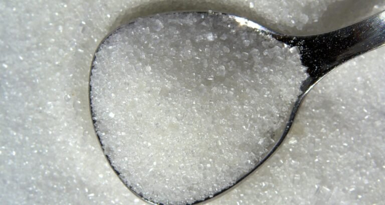Detailed macro shot of white sugar crystals on a reflective spoon.