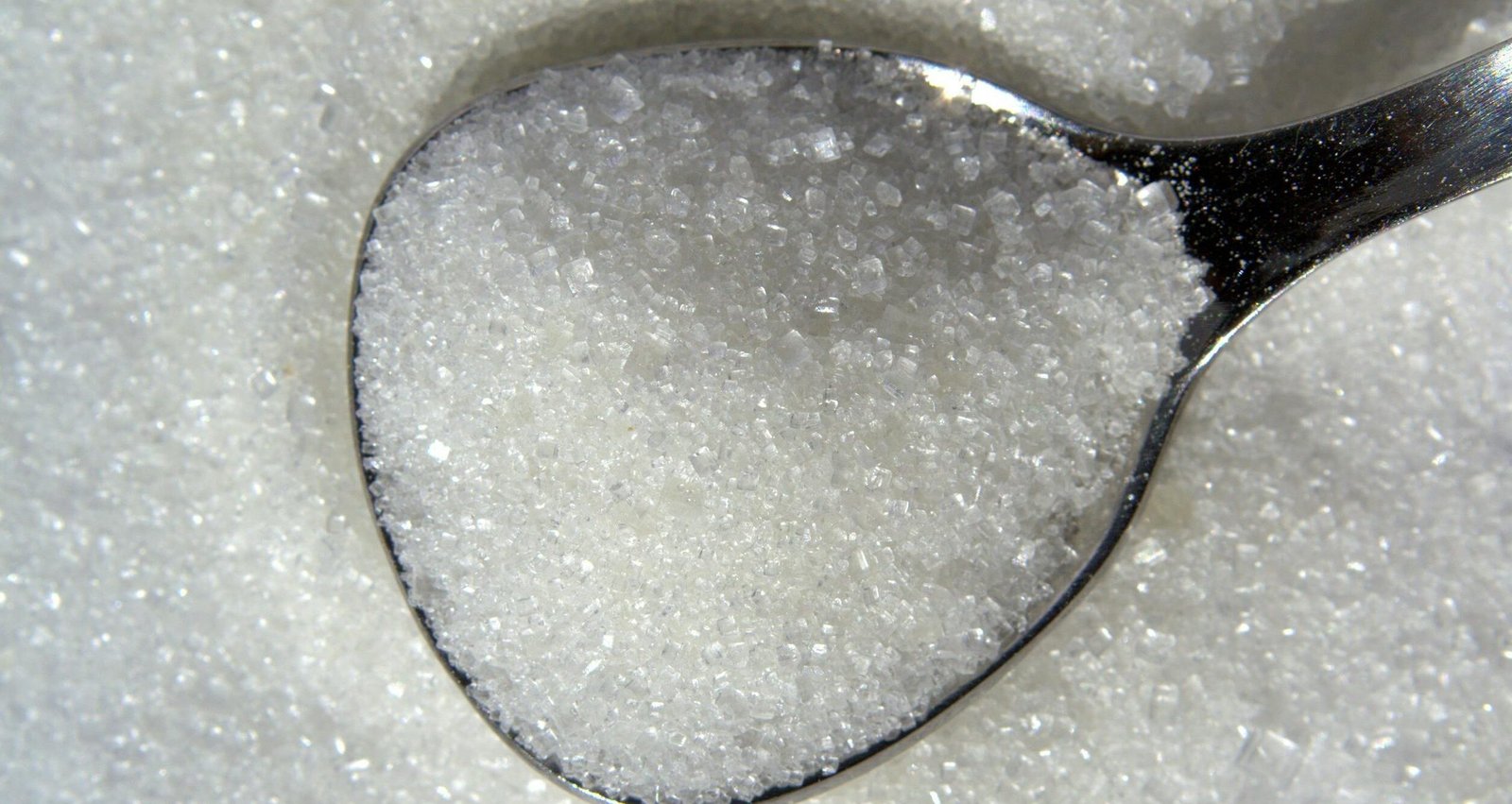 Detailed macro shot of white sugar crystals on a reflective spoon.
